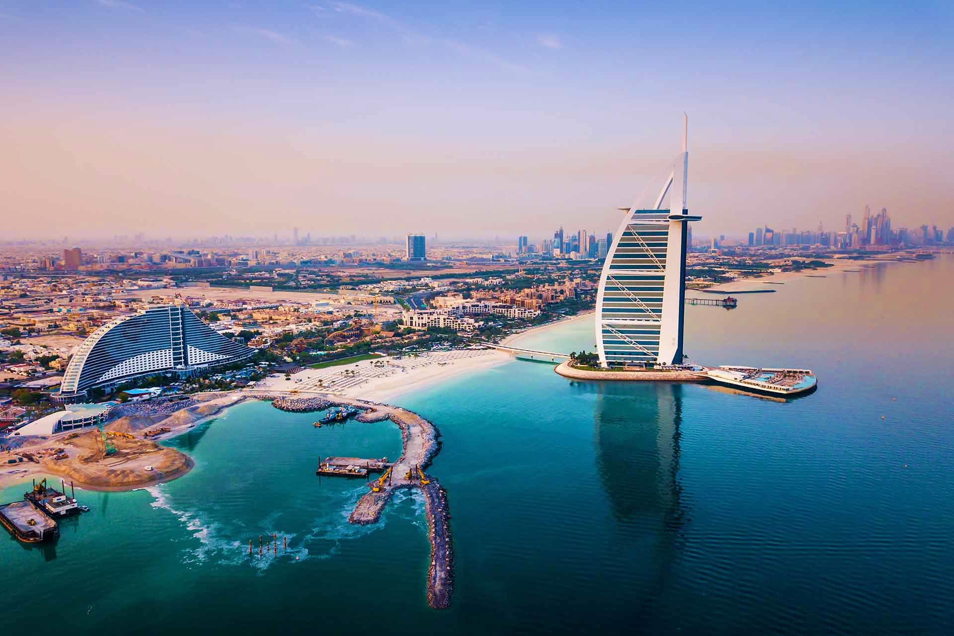 Aerial view of Burj Al Arab and Jumeirah Beach Hotel with Dubai skyline and turquoise waters